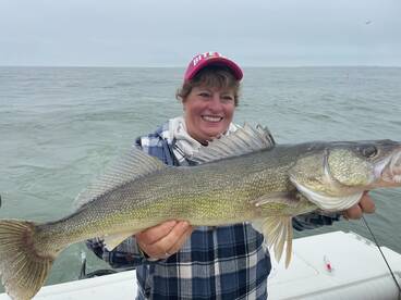 A proud angler holding a large Walleye while fishing on a boat, showcasing a successful catch in a scenic water environment.
