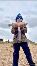 A young angler proudly displaying a Rainbow Trout against a scenic backdrop after a successful fishing trip.