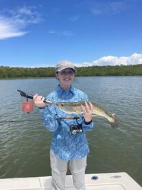 A young angler proudly displaying a Speckled Trout while fishing on a sunny day in a scenic waterway.