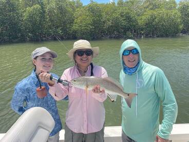 A family proudly displaying a Redfish caught during their fishing trip in a mangrove area.