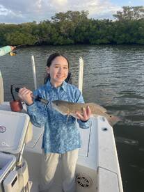 A young angler proudly holding a Redfish while fishing in a scenic mangrove setting.