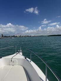A scenic view from the bow of a boat, showcasing the calm waters and coastal homes under a bright blue sky.
