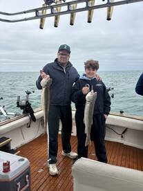 A father and son proudly displaying their catch of two Lake Trout while fishing on a boat, showcasing a memorable family fishing experience.