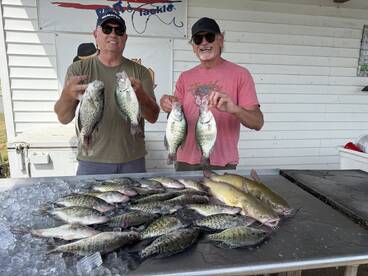 Two anglers proudly displaying their catch of Crappie and Catfish on a table after a successful fishing trip.