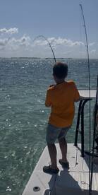 A young angler is actively reeling in a fish while fishing from a boat in clear waters, showcasing the excitement of the catch.