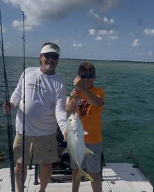A young angler and an adult proudly displaying a caught fish while fishing on a boat in clear waters.