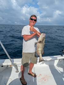 Angler proudly displaying a large Grouper while fishing offshore, showcasing a successful day on the water.