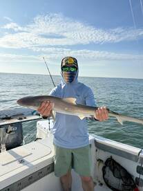 Angler proudly displaying a caught shark while fishing on a boat in open waters.