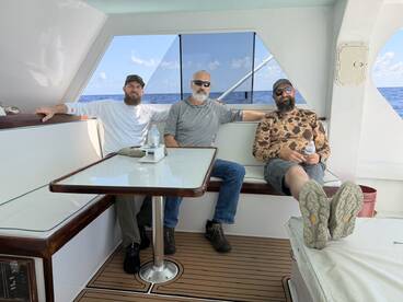 Three anglers relaxing inside the cabin of a spacious fishing boat, enjoying the ocean view.