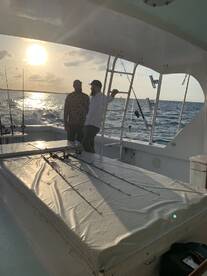 Two anglers enjoying a sunset on a fishing boat, with fishing rods ready for action.