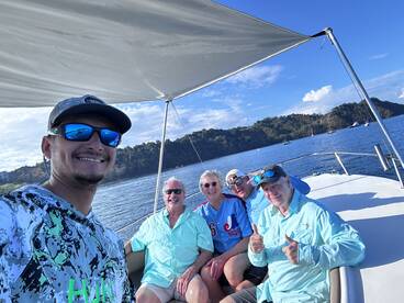 A cheerful group of four anglers enjoying their time aboard a fishing boat, surrounded by scenic waters and hills.