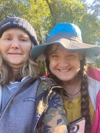 Two women smiling for a selfie in a natural setting, possibly enjoying a fishing trip.