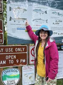 A woman points to a fishing regulations sign at Oxbow Regional Park, showcasing various salmon species and their seasonal availability.