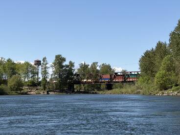 A scenic view of a river with a bridge and water tower, surrounded by lush greenery.