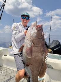 Angler proudly displaying a large Grouper on a fishing charter in open waters, showcasing a successful catch.