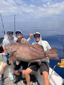 Three anglers proudly displaying a large Red Snapper aboard a fishing boat in clear blue waters.