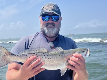 Angler proudly displaying a large Speckled Trout while fishing in the open water.