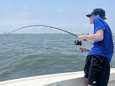 A young angler actively reeling in a fish while fishing from a boat in open water, showcasing the excitement of the catch.