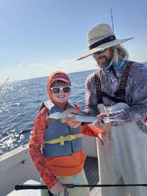 A young angler proudly holds a fish while fishing with an adult on a boat, showcasing a fun day on the water.