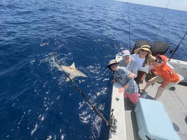A group of four anglers enjoying a thrilling moment while fishing for sharks in deep blue waters, showcasing camaraderie and excitement.