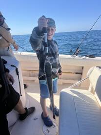 A young angler proudly displaying a caught fish aboard a fishing boat, enjoying a day on the water.