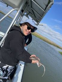 A young angler smiles while holding a small shark during a fishing trip in a scenic waterway.