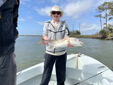 A young angler proudly displaying a Redfish while fishing from a small boat in a scenic coastal environment.