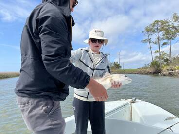 A young angler proudly holds a Redfish while fishing in a scenic coastal environment.