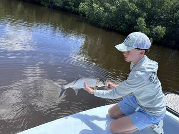 A young angler carefully holding a Silver Tarpon while fishing in a calm waterway, showcasing the excitement of youth fishing adventures.