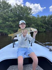 A young angler proudly displaying a Snook caught while fishing from a boat in a mangrove area.