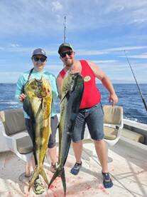 Two anglers proudly displaying their catch of Mahi Mahi aboard a fishing charter in open waters.