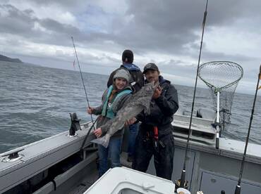 A young angler proudly holds a large fish while fishing on a boat, showcasing a successful catch in a coastal environment.