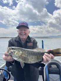 An enthusiastic angler proudly displaying a large Largemouth Bass while fishing on a scenic lake.
