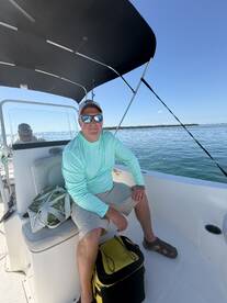 A relaxed angler seated inside a boat, enjoying a sunny day on the water, with a cooler and personal items nearby.