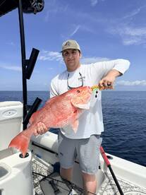 Angler proudly displaying a large Red Snapper while fishing on a boat in open waters.