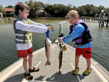 Two young anglers proudly displaying their catches of Redfish while enjoying a sunny day on the water.