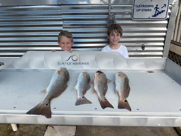 Two young anglers proudly displaying their catch of four Redfish on a cleaning table at a marina.
