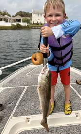 A young angler proudly displaying a large striped bass while fishing from a boat, showcasing a fun day on the water.