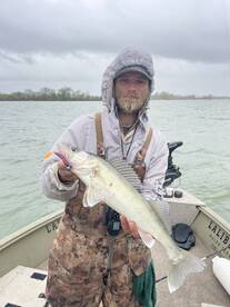 Angler proudly displaying a large Walleye while fishing on a cloudy day, showcasing the excitement of freshwater fishing.
