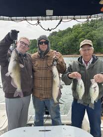 Three anglers proudly displaying their catch of catfish and crappie while enjoying a day on the water.