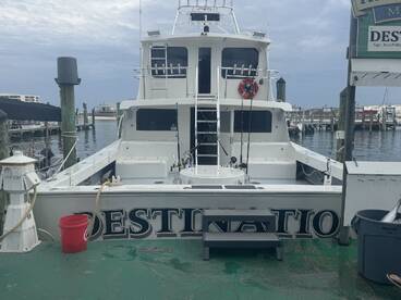 The exterior view of the fishing charter boat 'Destination' docked at the marina, showcasing its spacious design and fishing gear.