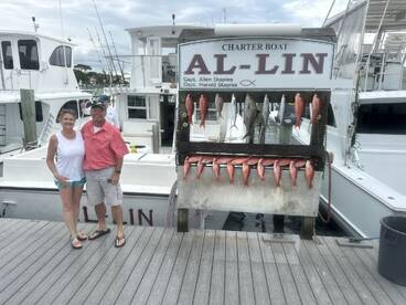 A couple poses in front of a catch board displaying a variety of fish, including Snapper, after a successful fishing trip on the charter boat Al-Lin.