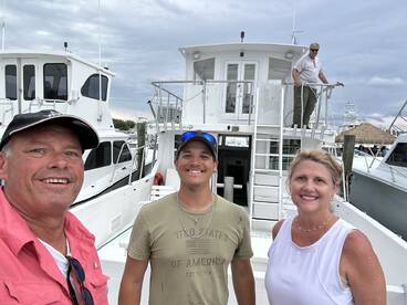 A group of three smiling individuals on the deck of a fishing charter boat, showcasing a friendly atmosphere before their fishing adventure.