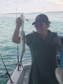 Angler proudly displaying a fish while fishing on a boat in clear waters.