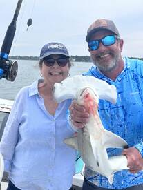 Two anglers proudly displaying a large shark while enjoying a fishing trip on the water.