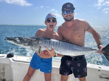 Two anglers proudly displaying a large Wahoo while fishing in clear blue waters.