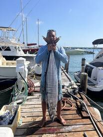 Angler proudly displaying a large Wahoo on the dock after a successful fishing trip.