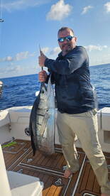Angler proudly displaying a large fish on the deck of a boat during a deep-sea fishing trip.
