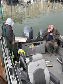 Two anglers on a boat, one preparing fillets while the other relaxes, with several fish laid out on the deck after a fishing trip.