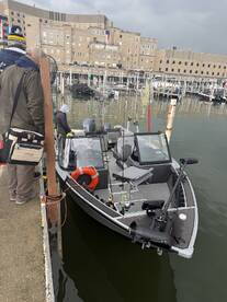 A group of anglers preparing to board a sleek fishing boat at the marina, showcasing the boat's exterior and fishing gear.